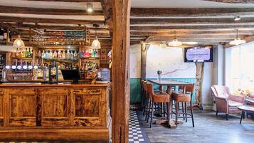 Un rústico espacio de bar con mostrador de madera, estantes llenos de botellas de licor y lámparas colgantes.