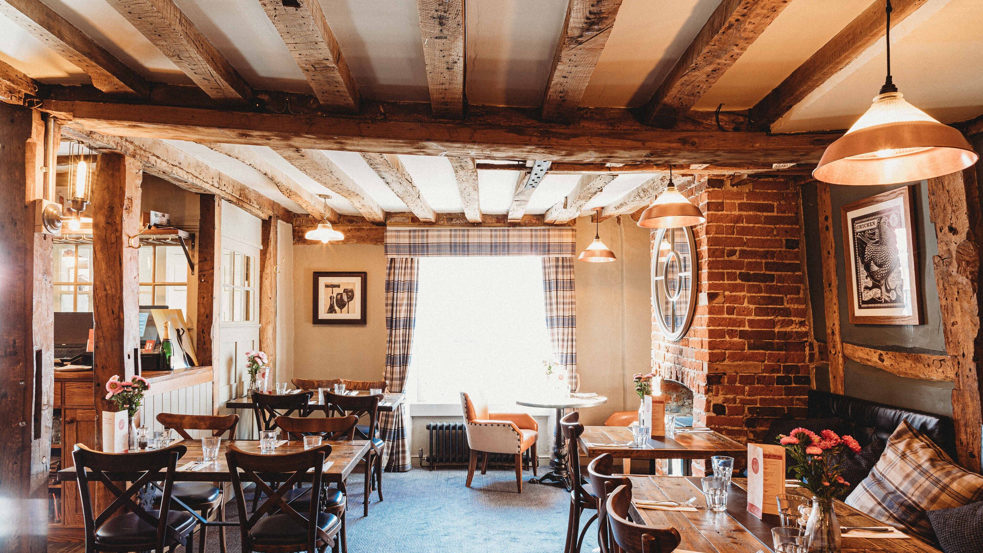 A rustic dining area with wooden beams, brick walls, and a mix of wooden and upholstered furniture.