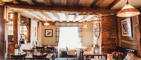 A rustic dining area with wooden beams, brick walls, and a mix of wooden and upholstered furniture.