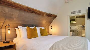 A bedroom with a wooden headboard, a bed with white bedding and mustard pillows, bedside lamps, and a bathroom visible through an open door.