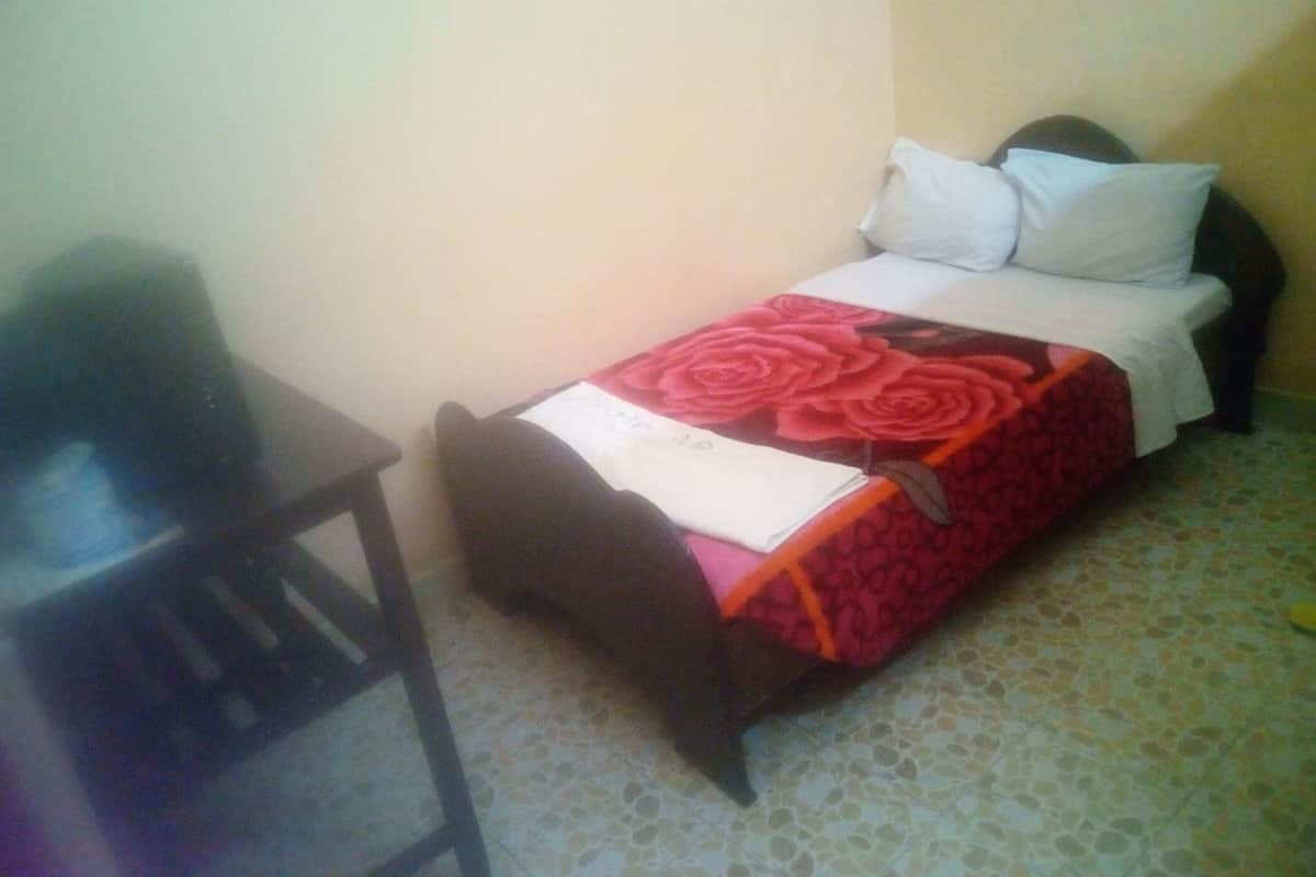 A small, single-bed room with a wooden headboard, a bedside table, and a patterned bedspread.