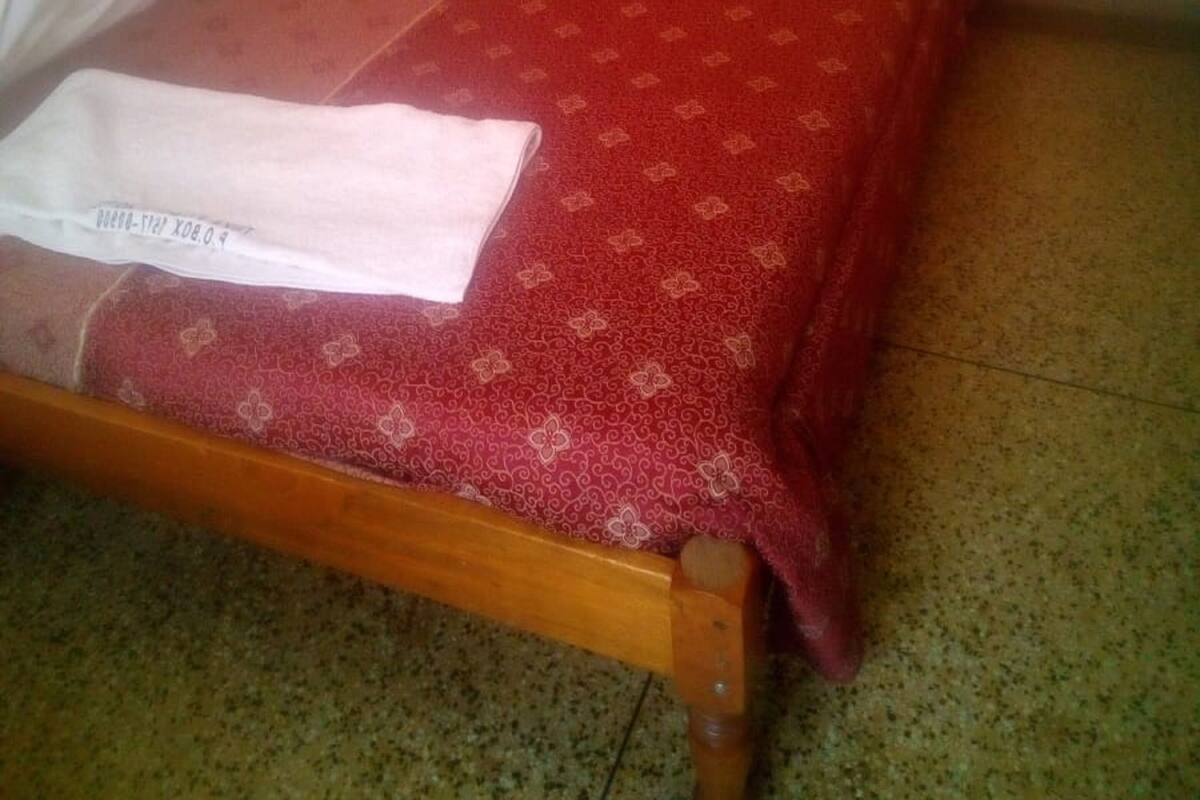 A bed with a red patterned bedspread and a white pillow.