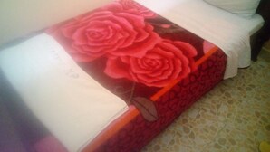 Una cama con colcha floral, almohadas blancas y una manta blanca.