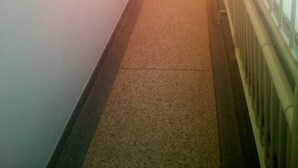 Un pasillo estrecho con paredes blancas, suelo alfombrado y barandilla de metal a la derecha.