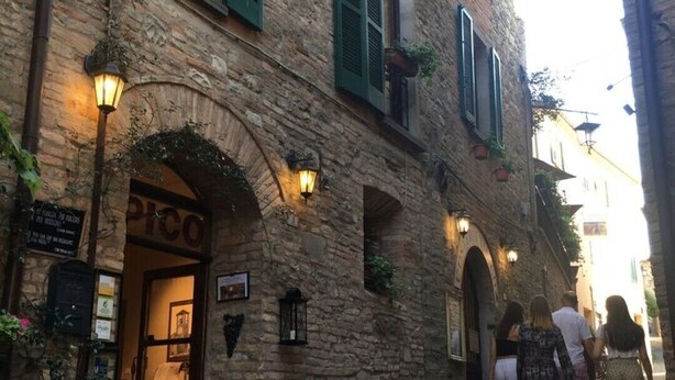 Una stretta via acciottolata con un edificio in pietra caratterizzato da portali ad arco e persiane verdi.