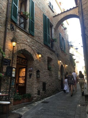 A narrow cobblestone street with a stone building featuring arched doorways and green shutters. - Villa on Umbria Tuscany border, sleeps 12, stunning infinity pool superb views, (Montone PG)