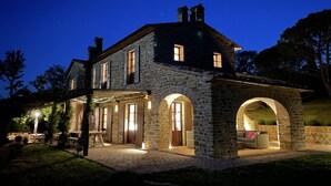 Una casa in pietra con un portico coperto e aperture ad arco, illuminata da luci interne.