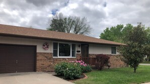 A single-story house with a garage, brick exterior, and a front porch with pink flowers.
