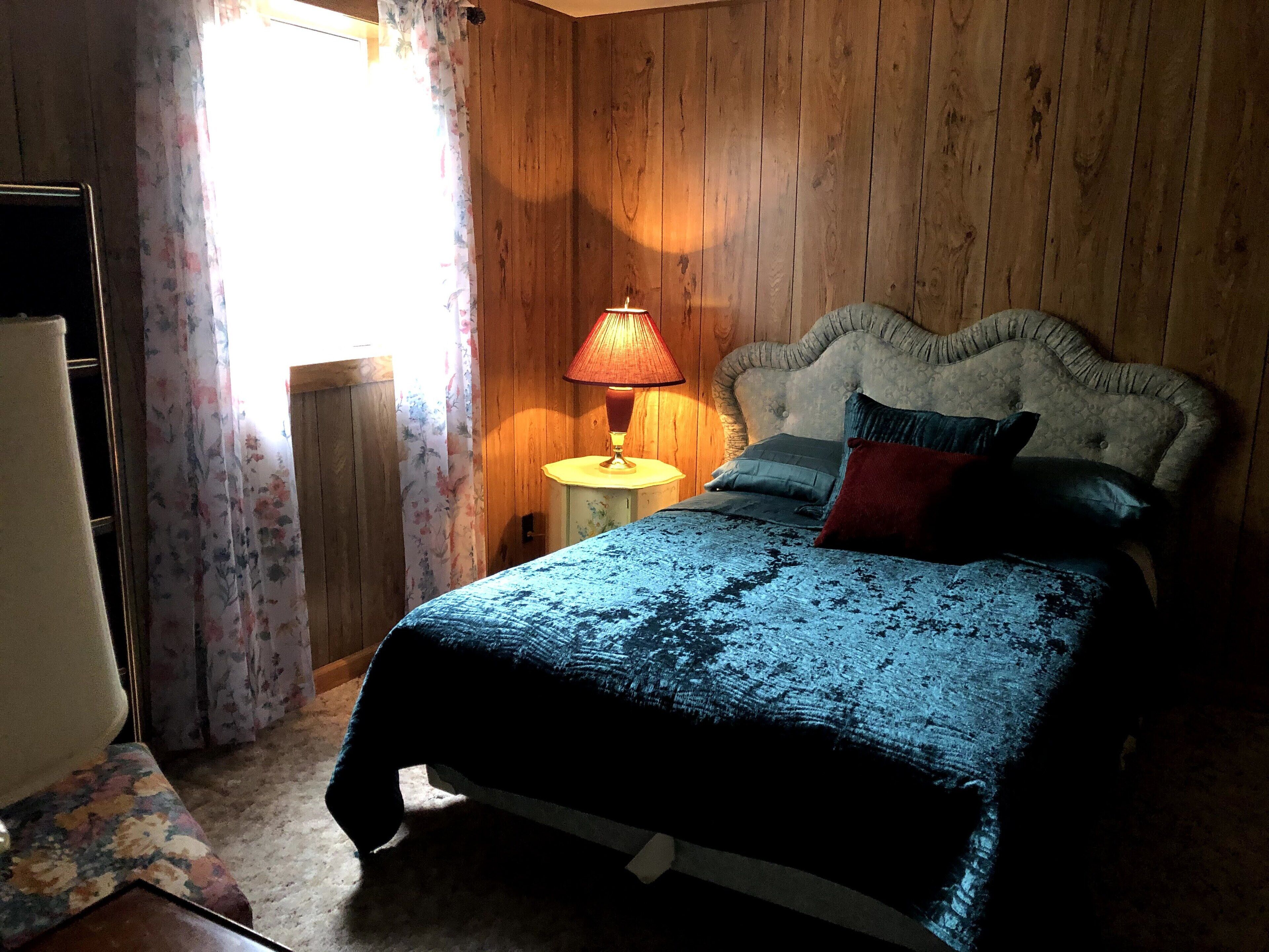 A bedroom with a wooden headboard, a bed with a blue textured bedspread, and a nightstand with a lamp.