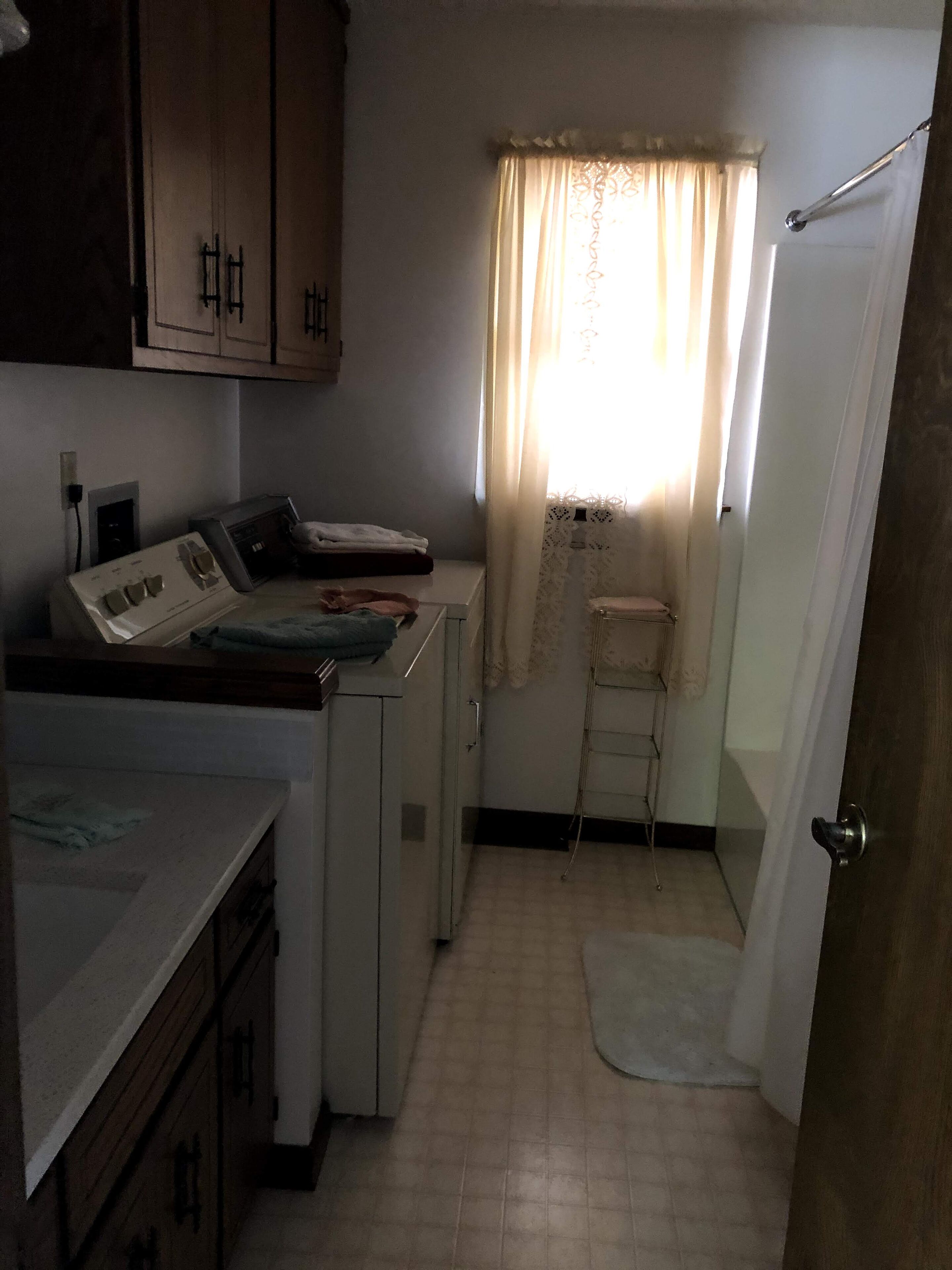 Una cocina compacta con electrodomésticos básicos, una pequeña ventana con cortinas, y una puerta que da a otra habitación.