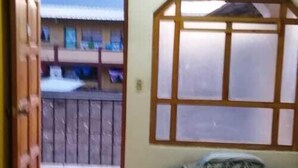 A bedroom with a bed, a window with a wooden frame, and a view of a balcony. - Posada el mesón xela (Quetzaltenango)