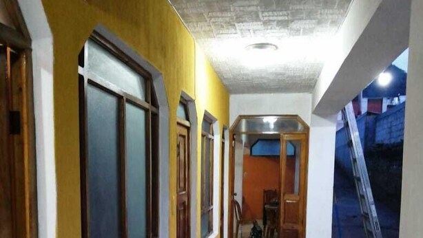 A corridor with yellow walls and tiled flooring, leading to a room with a wooden door and a window. - Posada el mesón xela (Quetzaltenango)