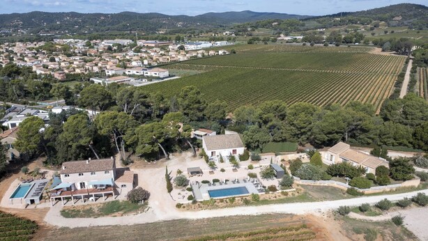 An aerial view of a residential area with a large house featuring a swimming pool, surrounded by vineyards and a small town in the background. - Gîte Villa Sous Les Pins (LA LONDE LES MAURES)
