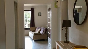 A hallway with a sofa in the background, a mirror, and a table with books. - Gîte Villa Sous Les Pins (LA LONDE LES MAURES)