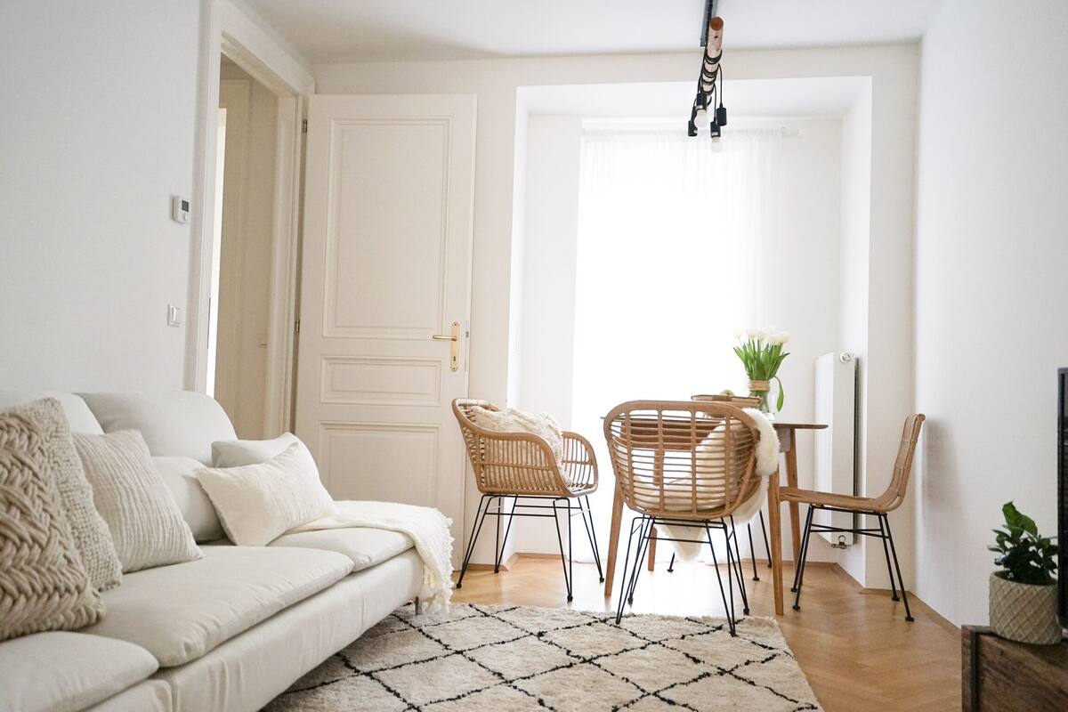 A modern living room with a white sofa, two wicker chairs, a coffee table, and a patterned rug.