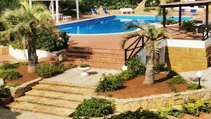 A swimming pool with a pergola, lounge chairs, and a stone pathway.