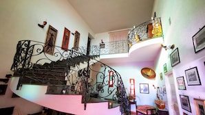A spiral staircase with ornate metal railings, a cushioned bench, and a wall adorned with framed pictures.