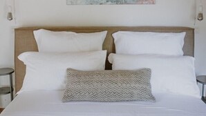 Ein Schlafzimmer mit Holzbalkendecke, einem Bett mit weißer Bettwäsche, zwei Nachttischen und einem an der Wand hängenden abstrakten Gemälde.