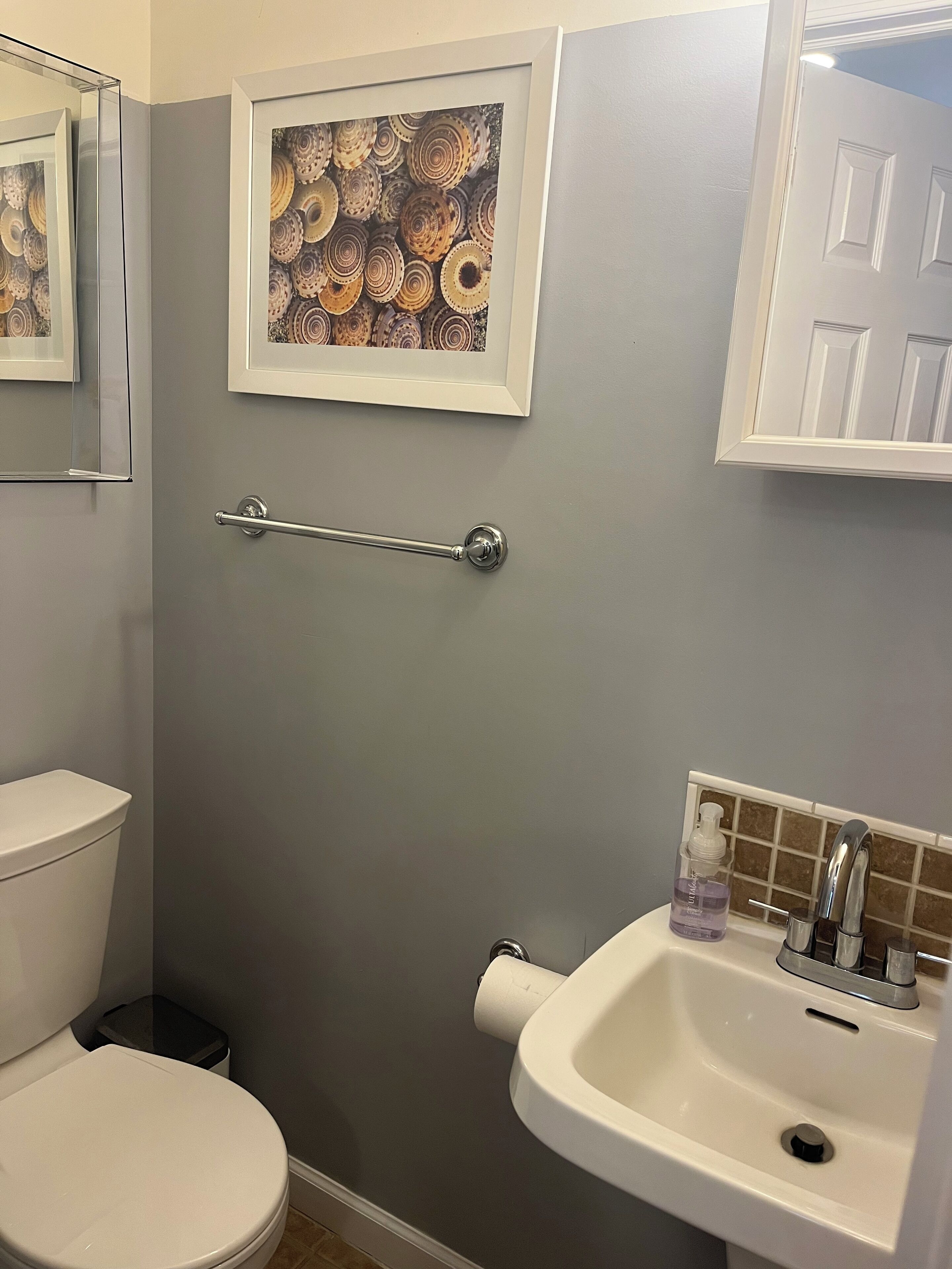 A bathroom with a toilet, sink, and framed artwork on the wall.