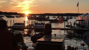 A marina with boats docked, a sunset in the background, and a flag on a pole.
