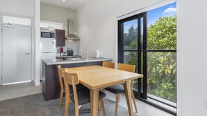 Une cuisine moderne dotée d’un îlot central, d’un coin repas avec une table et des chaises en bois, et d’une grande porte-fenêtre coulissante donnant sur un balcon agrémenté de plantes.