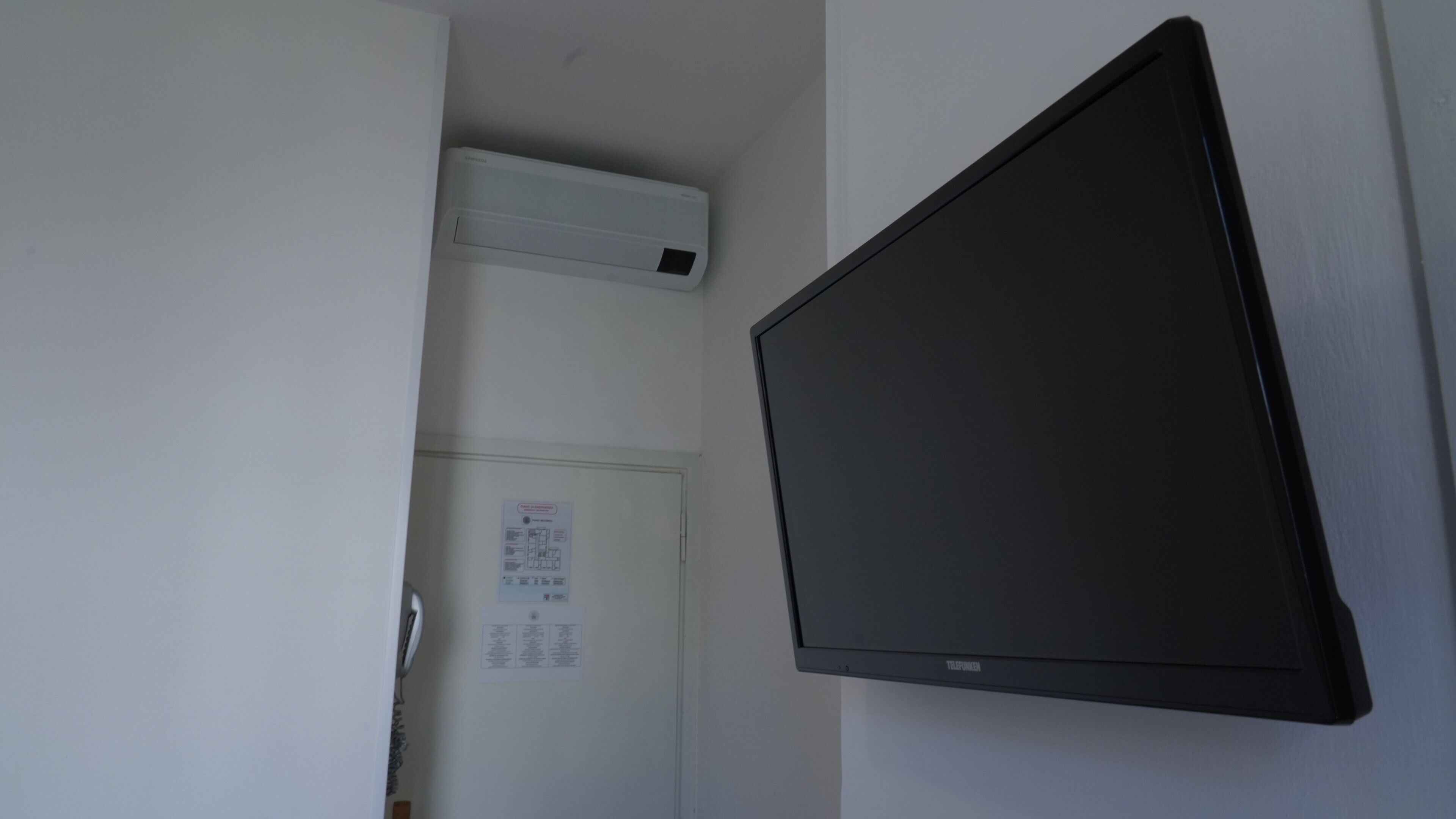 Una habitación con un televisor de pantalla plana montado, un equipo de aire acondicionado blanco y una puerta con un aviso.