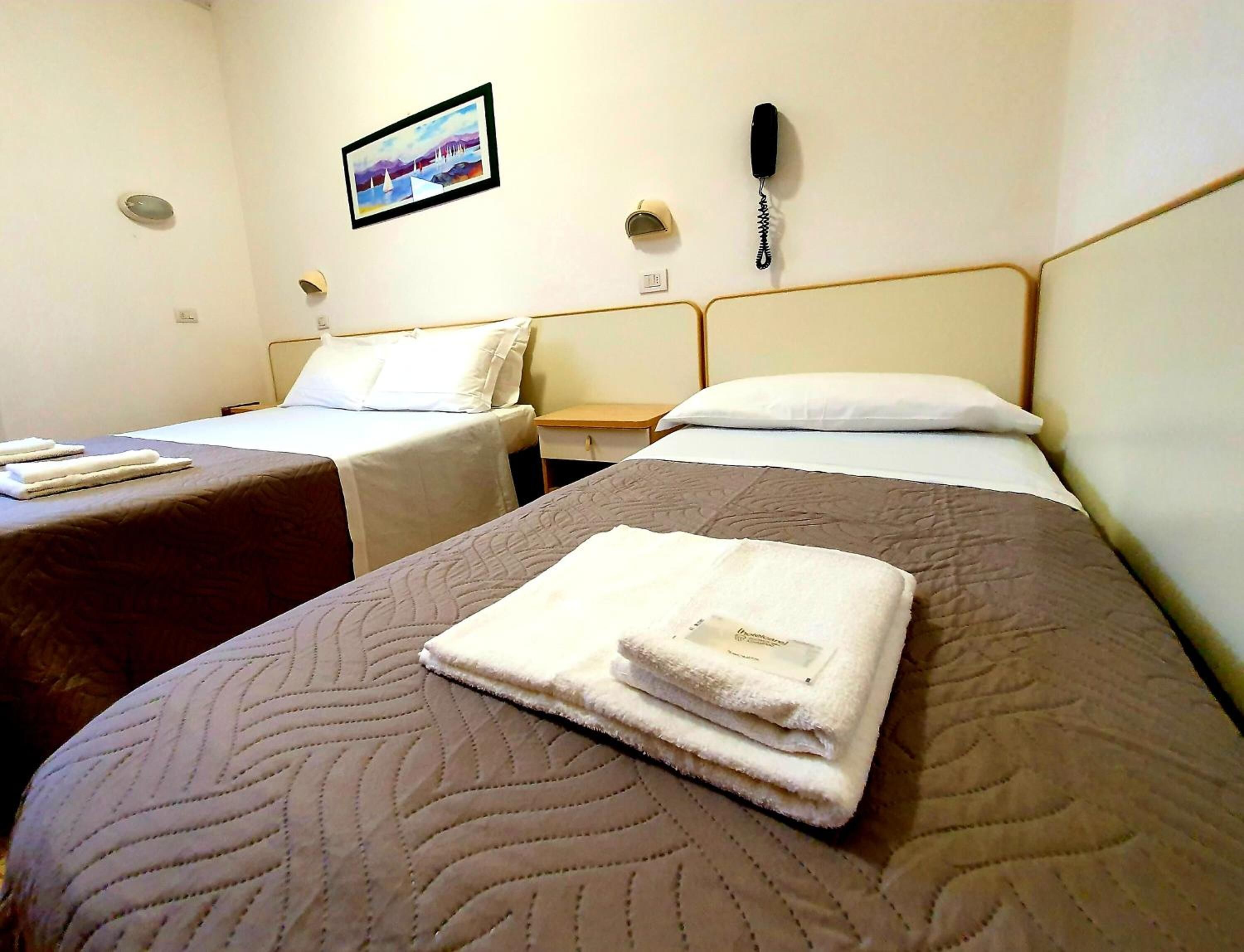 A hotel room with two beds, a painting on the wall, a phone, and a small table.