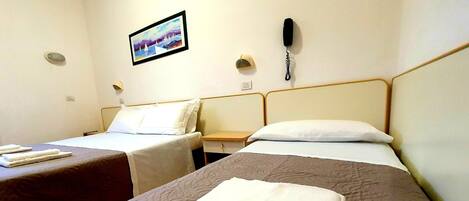 A hotel room with two beds, a painting on the wall, a phone, and a small table.