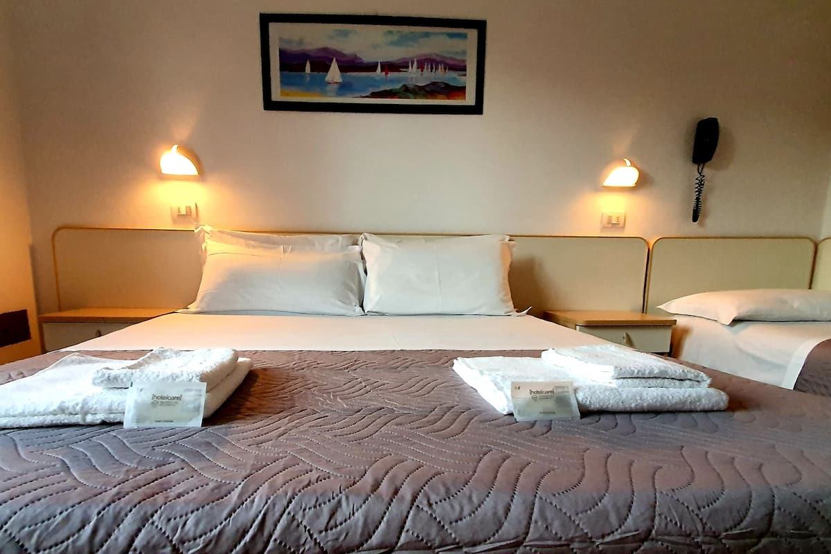 A hotel room with a large bed, two bedside tables, a painting on the wall, and a phone on the wall.