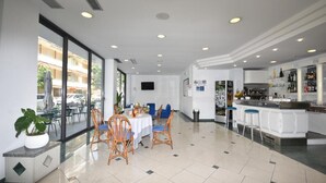 A modern hotel lobby with a dining area, a bar, and a kitchen visible in the background.