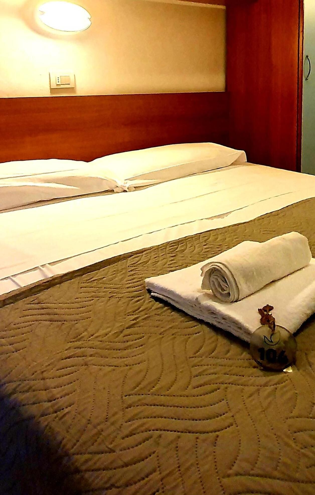 A hotel room with a bed, a rolled towel, and a small decorative item on the bed.