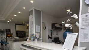 A reception desk with a white counter, a blue vase with flowers, and a clock on the wall.