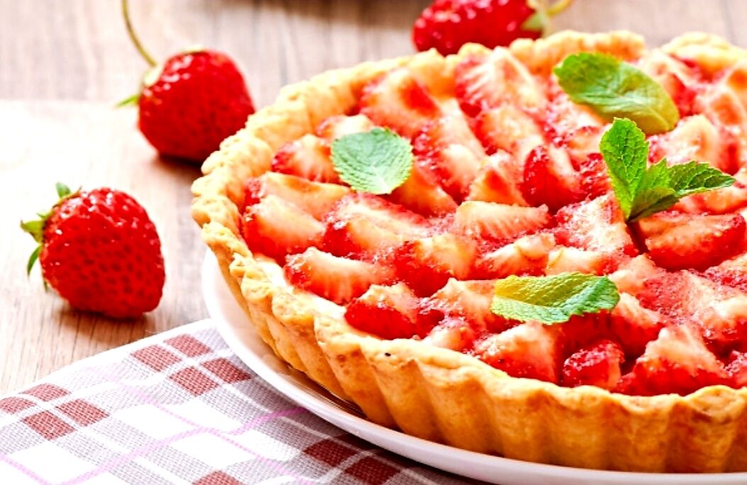 Una tarta de fresas con hojas de menta sobre un plato blanco.