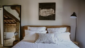 A bedroom with a wooden headboard, white bedding, a large mirror, and a black lamp.