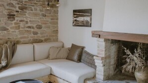 A cozy living room with a stone wall, a fireplace, a white sofa, and a patterned rug.