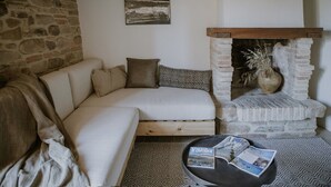 A cozy living room with a stone wall, a white sofa with patterned cushions, a fireplace, and a round coffee table with a magazine.