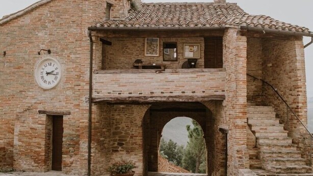 A rustic building with a brick facade, a clock, and a staircase leading to a balcony.