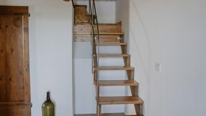 A wooden staircase with a rustic design, leading to a landing area with a wooden door and a green bottle on the floor.
