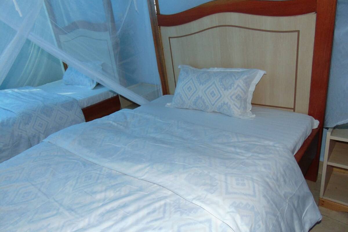 Quarto com duas camas, cada uma com colcha branca e travesseiro estampado.