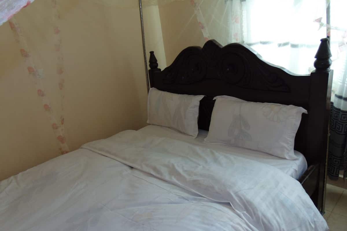 Cama com lençóis brancos e cabeceira de madeira escura em quarto com papel de parede floral.