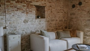 Una habitación rústica con paredes de ladrillo visto, un sofá blanco, una pequeña mesa blanca y una lámpara colgante.