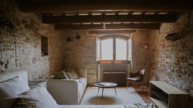 Una habitación rústica con paredes de ladrillo visto, una cama, un sofá, una pequeña mesa redonda y una chimenea.