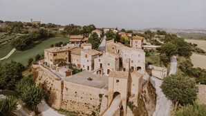 Un edificio histórico de piedra con varias estructuras, incluyendo una torre, rodeado de vegetación y un sendero.