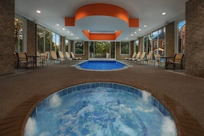 Ein Wellnessbereich mit Whirlpool und Schwimmbad, umgeben von Liegestühlen und einer Ziegelwand.