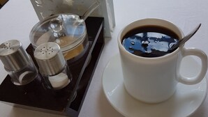 Una taza blanca de café sobre un plato, con una cuchara, un azucarero y un salero en una bandeja.