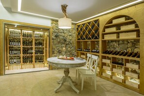 A wine cellar with wooden shelves and a stone wall, a round table with chairs, and a chandelier.