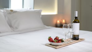 Cama bem arrumada com lençóis brancos, uma tigela de morangos, duas taças de vinho e uma garrafa de vinho em um suporte.