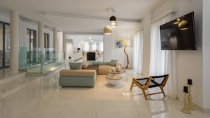 A spacious living area with a large sofa, a coffee table, and a TV mounted on the wall. - Phaos at Cellaria Estate (Santorini)