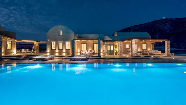 A luxurious poolside area with a clear view of a large building, outdoor seating, and a mountain backdrop. - Phaos at Cellaria Estate (Santorini)