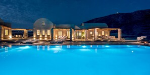 Un espace de détente luxueux au bord de la piscine, offrant une vue dégagée sur un grand bâtiment, avec des sièges extérieurs et une chaîne de montagnes en arrière-plan.